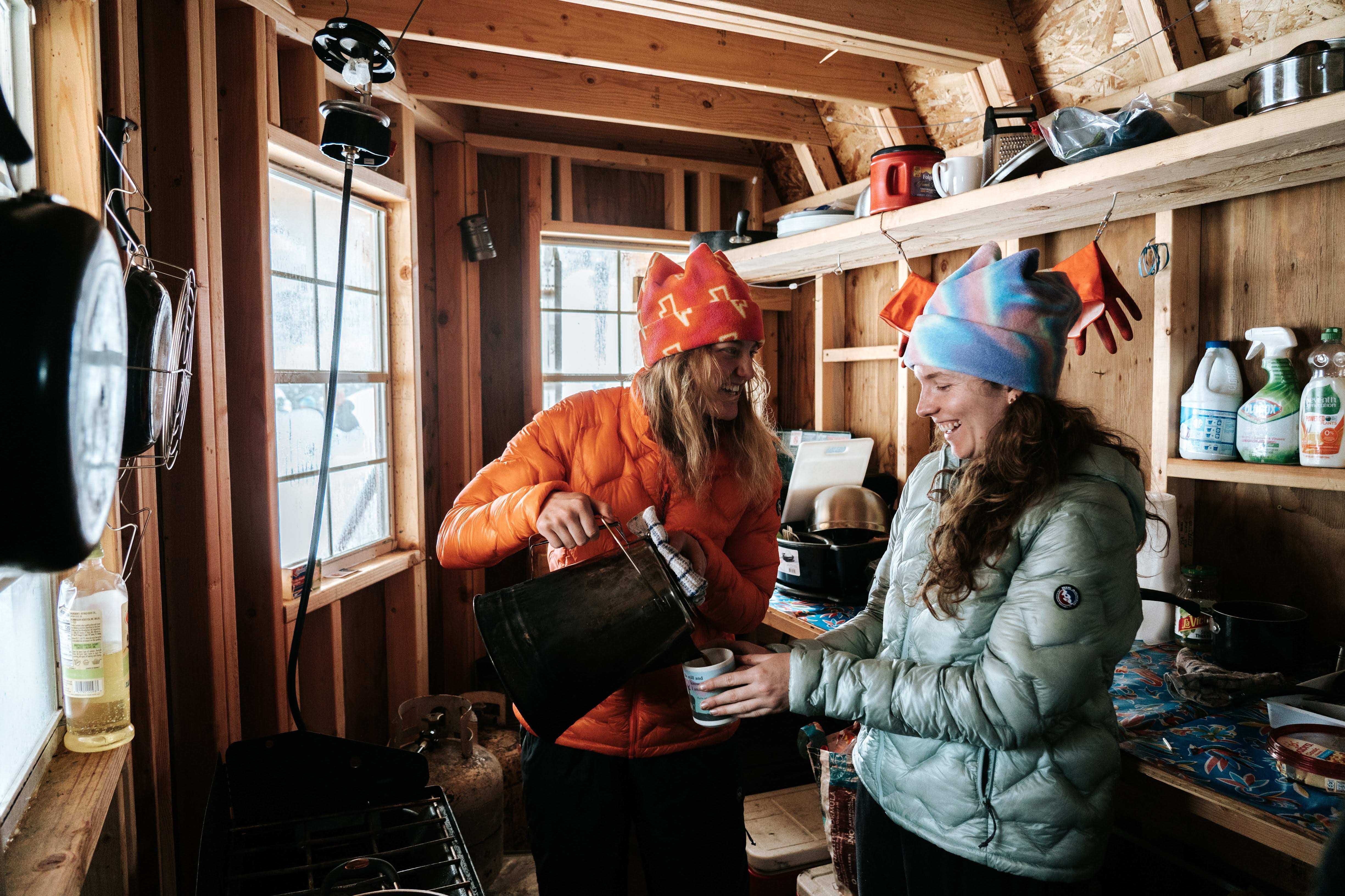 Pouring coffee in a backcountry hut, wearing Bearsley and Piney Mountain jackets