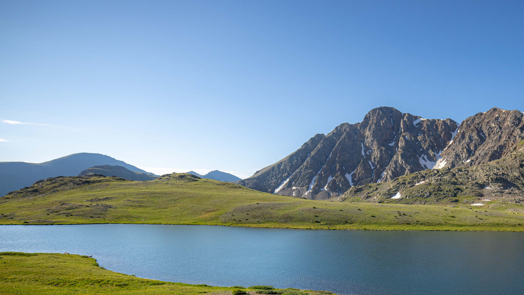 A lake with rolling hills, and mountains in the background