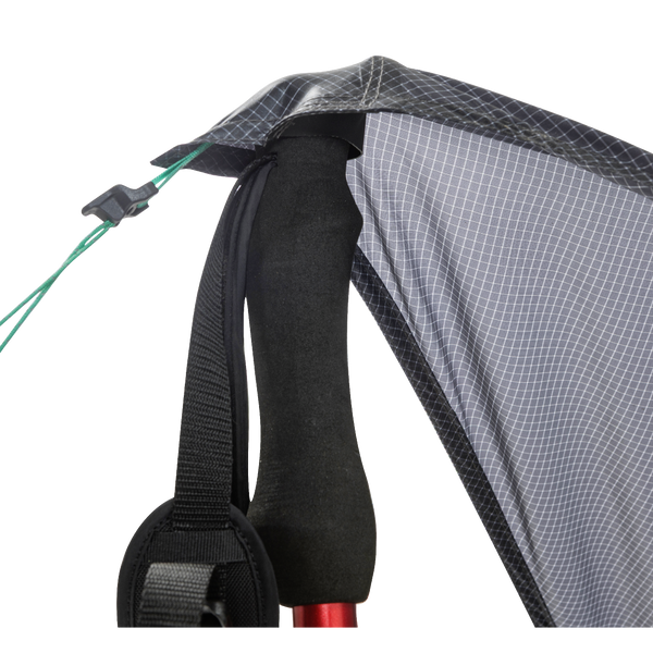 Close-up of the Big Agnes String Ridge VST 1.5, with a trekking pole supporting the tent’s black and gray fabric corner, black strap, and green guyline with a plastic tensioner in this ultralight shelter setup.